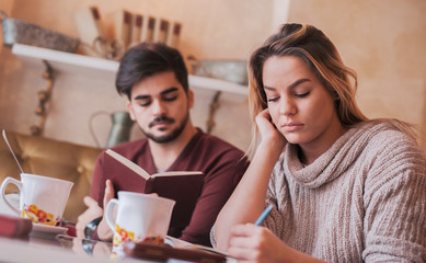 Young couple drinking coffee and reading a book in the cafe. Education, relationships, love concept