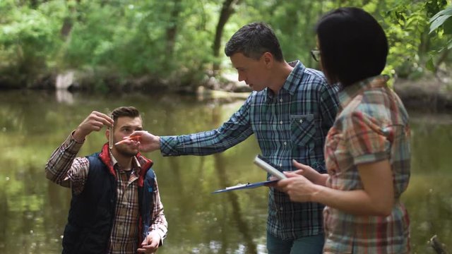 Three ecologists wearing casual clothing exploring lake and taking water sample.