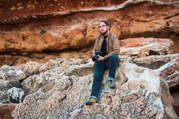 Young male photographer sitting on a rock beach with camera in his hands