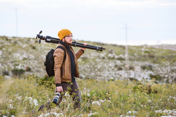 Fototapeta premium Young photographer walking in the nature with tripod on his shoulder and camera in hand
