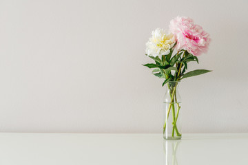 Bouquet of white and pink peonies in glass vase on white background