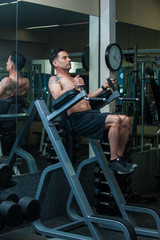 Muscular middle age man in gym on Roman Chair with knees lifted.