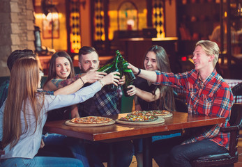 Friends having a drinks in a bar, They are sitting at a wooden table with beers and pizza.
