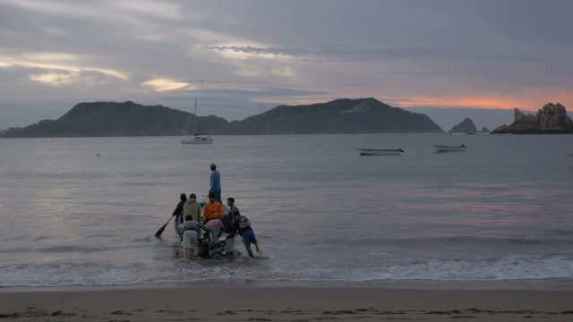 A group of men get into a boat from shore and go out towards sea during sunrise