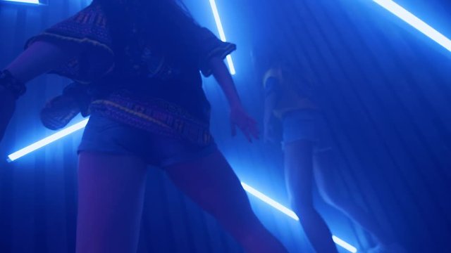 Young women dancing in disco light at nightclub. Two girls energy dance on neon lamps background. Sexy women shaking buttocks in slow motion. Women dance with neon lighting at disco club. Nightlife