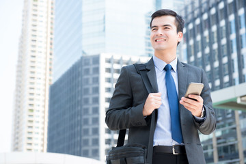 Fototapeta premium Smiling businessman using mobile phone while carrying bag and walking in the city