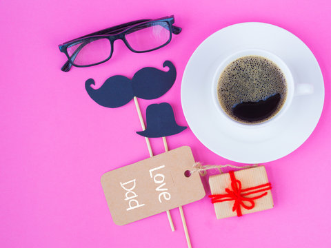 Father's day concept. LOVE DAD message with pink flower, black glasses, coffee cup, gift and black Mustache on pink background