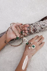 Nahaufnahme von Frauenhänden, die eine ethnische Halskette mit Sandhintergrund halten © zolotareva_elina