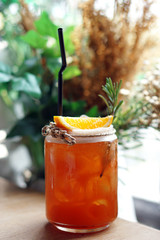 Glass of Iced tea with lemon slice topped with orange and rosemary leaves on blurred background, Selective focus.