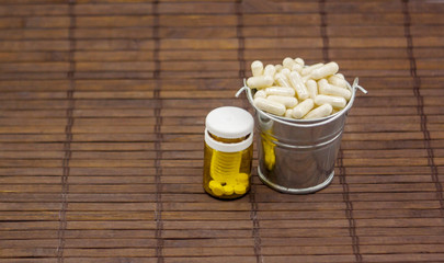 A large number of round tablets and capsules in a bucket on a dark wooden background