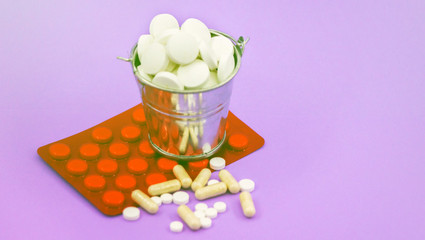 A full bucket of round tablets and a red packing of pills on a lilac background