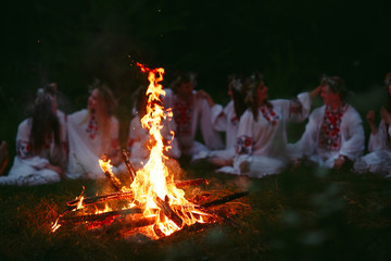Midsummer night. Young people in Slavic clothes sitting near the bonfire.