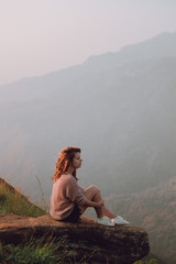 The girl sits on a stone with a view of the mountains