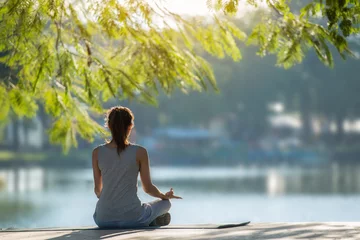 Fototapete Beautiful woman practicing yoga waterfront in the park. © sunti