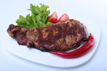 Pork ribs on grill and chili pepper with tomato, lettuce leaves on white plate