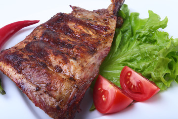 Pork ribs on grill and chili pepper with tomato, lettuce leaves on white plate
