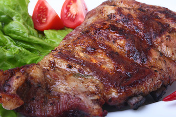 Pork ribs on grill and chili pepper with tomato, lettuce leaves on white plate