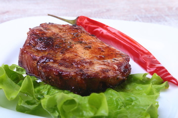 Steak of grilled meat and chili pepper with tomato, lettuce leaves on white plate.