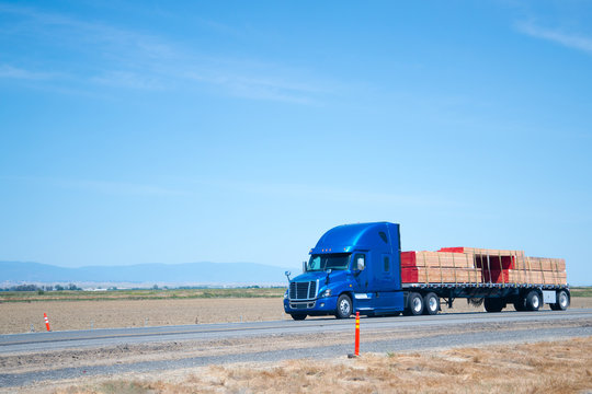 Big rig blue semi truck with flat bed trailer transporting lumber wood on flat road