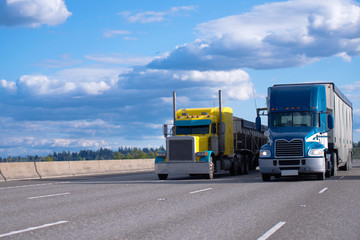 Classic yellow and blue modern semi trucks side by side on the road