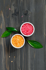 Top view of cosmetic pink and orange sea salt on a black wooden table.
