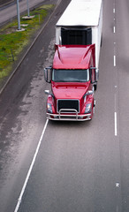 Modern red semi truck with refrigerator unit on reefer trailer driving on divided highway