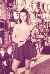 Girl standing in t-shirt in sporting goods store with racket