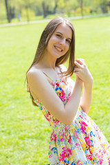 Portrait of young beautiful woman with long hair wearing flower dress in green spring park