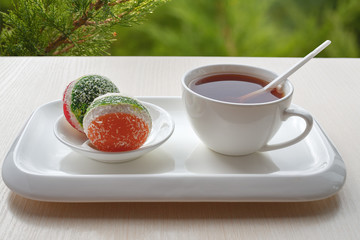 Cup of tea and candied fruit jelly in a white ceramic dish is on the table. Breakfast on a green background. Lifestyle. Selective focus. For culinary publishers and web sites.