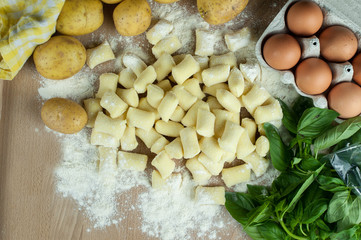 Uncooked gnocchi on flour table with gnocchi recipe basic ingredients: potatoes, eggs and flour.
