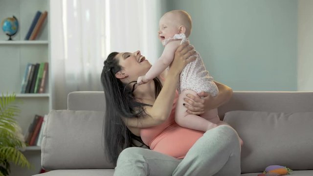 Excited young mother actively playing with her little daughter at home, family