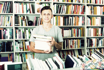 teenage boy with book pile in shop.