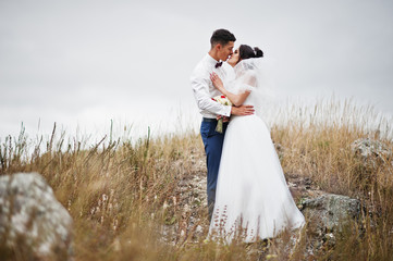 Fantastic wedding couple walking in the tall grass with the pine trees and rocks in the background holding hands.