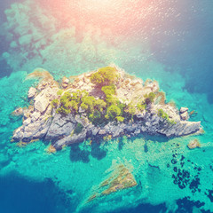 Top view of a rocky island with green trees in the sunlight