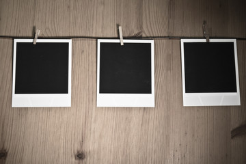 three blank instant photos hanging on clothesline on wooden background, art concept