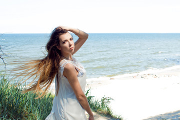 Fototapeta na wymiar Young charming brunette woman on sea coast. Beautiful girl in a short white summer dress