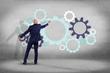 Businessman in front of a wall writing on a cog wheel interface - business concept