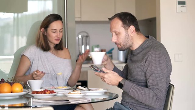 Couple fighting, arguing during meal at home, man using smartphone 
