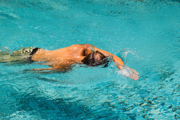 Young man is swimming in a transparent water of a pool in a sunny day.