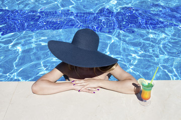 Beautiful woman in bikini and large hat relaxing at pool with cocktails. Summer holidays, travel, vacation concept. Copy space.