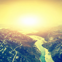 Top view of the river in the mountains surrounded by a green forest at sunset