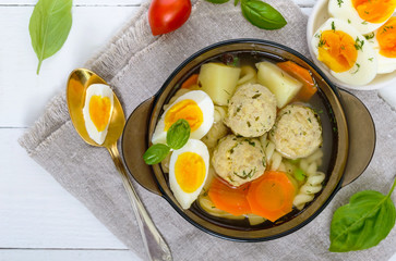 A bowl of soup with chicken meat balls, vegetables, boiled egg and fusilli. Top view.