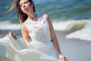 Fototapeta na wymiar Young charming brunette woman on sea coast. Beautiful girl in a white summer dress. Runs towards the sea