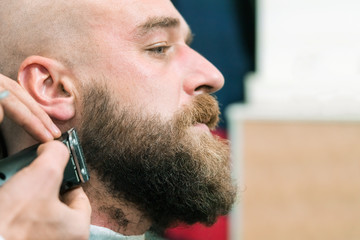 Young man while cutting his beard with a clipper