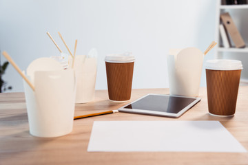 Close-up view of food boxes with chopsticks, disposable coffee cups and digital tablet on office table