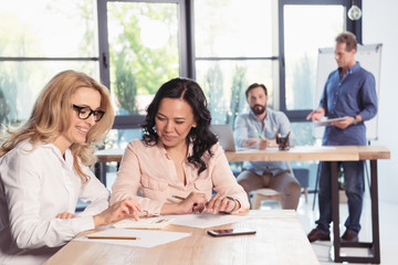 Beautiful smiling businesswomen sitting at table and working together in office