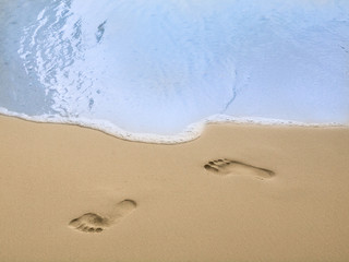 Fototapeta na wymiar Footprints on sand that will delete by a wave. The meaning of the photo is nothing last forever.