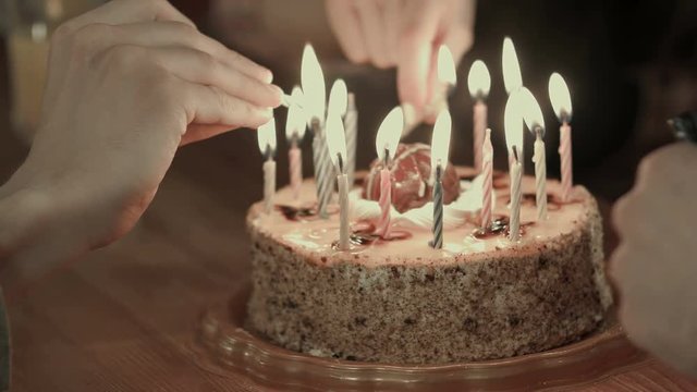 Two people lighting the candels on a birthday cake