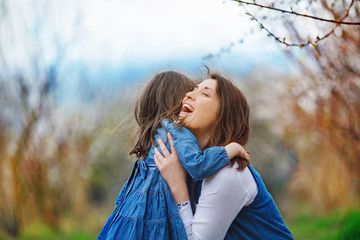Mom and daughter embrace in the midst of a flowering apricot garden. The woman squats and laughs,...