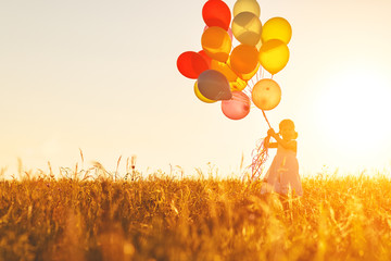 Happy cheerful child girl with balloons on meadow at sunset in summer.